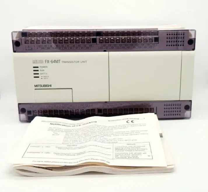 Mitsubishi FX-64MT-ESS compact PLC with transistor outputs, featuring 32 digital inputs and outputs, displayed with manual.
