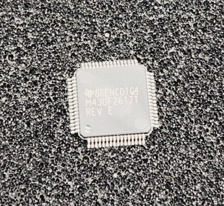 Texas Instrument MSP430F2617T PM Mixed-Signal Microcontroller LQFP-64 chip, top view on a textured surface