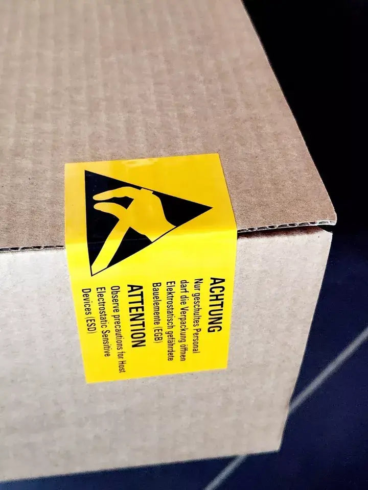 Sealed cardboard box with yellow caution tape labeled 'Attention' indicating ESD precautions.