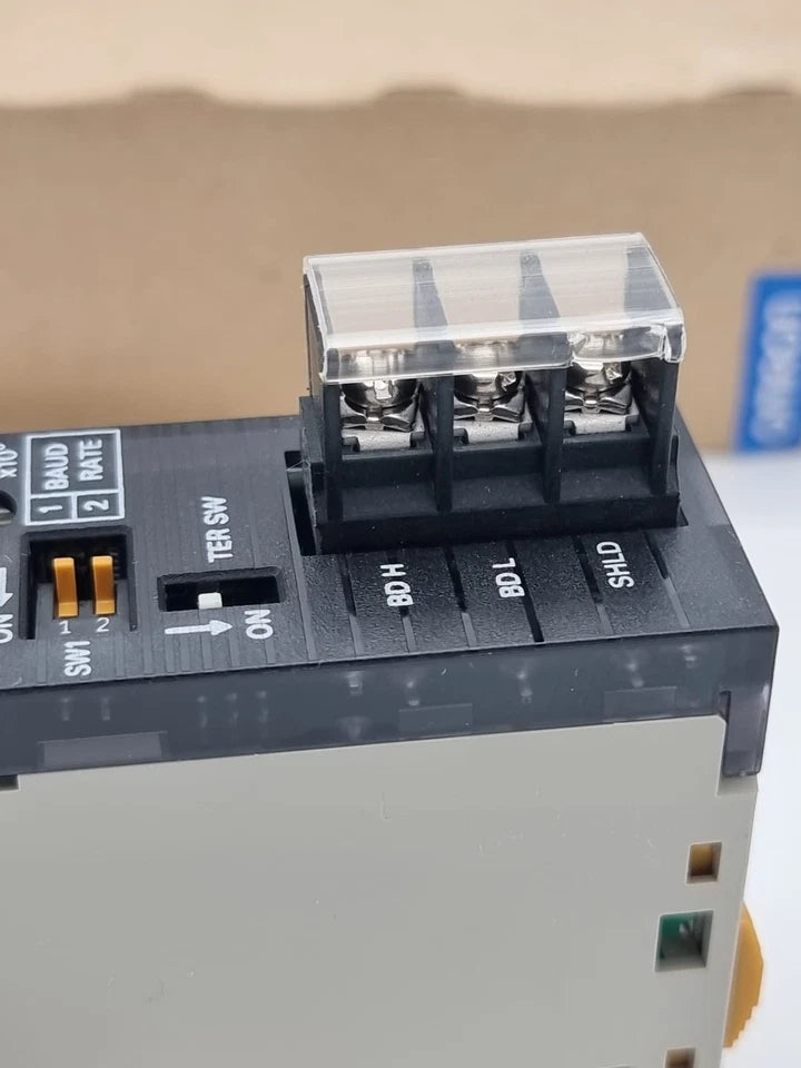 Omron CJ1W-CLK21-V1 Controller Link Kommunikationsmodul in Nahaufnahme, Originalverpackung im Hintergrund, SPS-Kommunikation